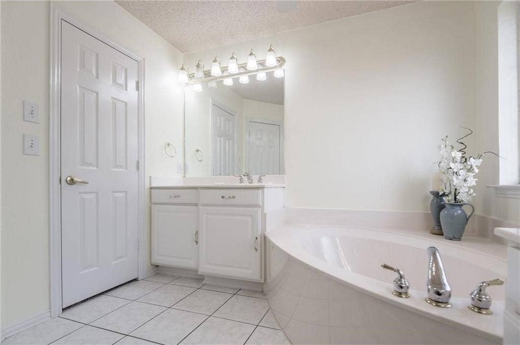 5000 Pointclear Court, Arlington, TX 76017 White paneled door, double vanity with white cabinetry, built-in bathtub with deck-mounted chrome fixtures, wall-mounted mirror, and tile flooring