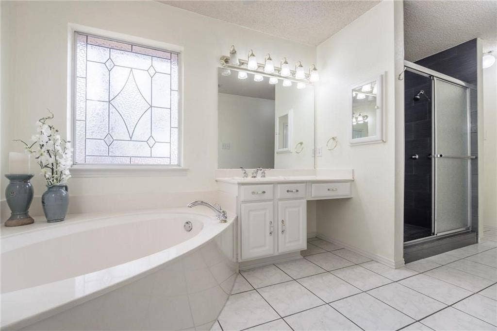 5000 Pointclear Court, Arlington, TX 76017 White tile flooring, built-in soaking tub, decorative privacy window, dual vanity with white cabinetry, and a glass-enclosed shower