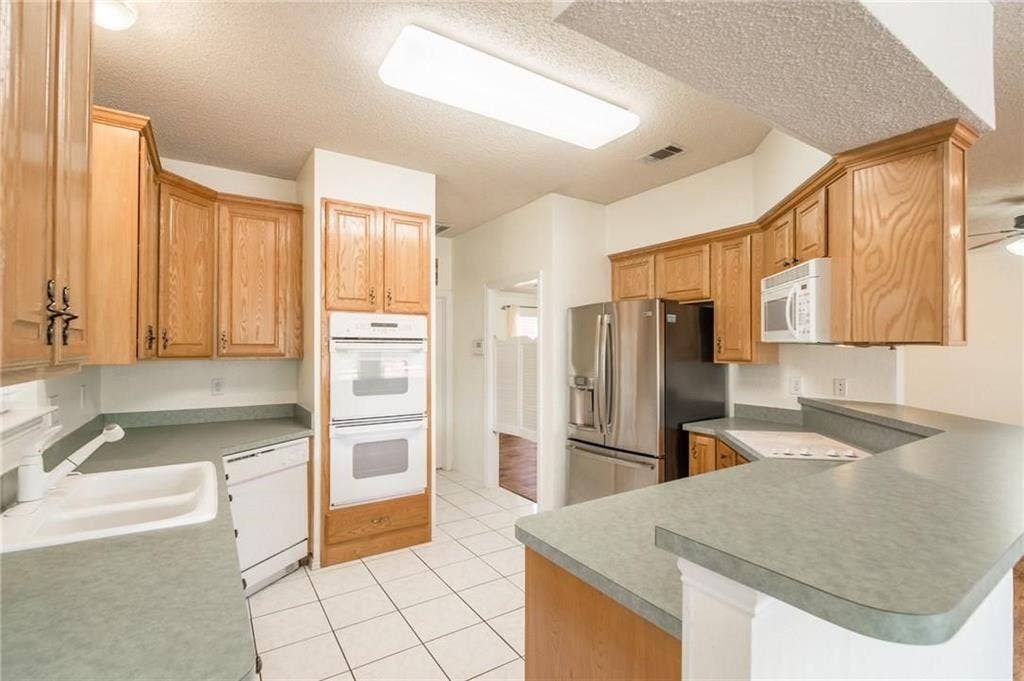 5000 Pointclear Court, Arlington, TX 76017 Kitchen featuring wood cabinetry, white tile flooring, stainless steel refrigerator, white double wall ovens, and a built-in cooktop