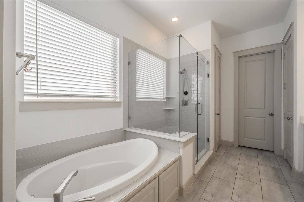 Freestanding oval soaking tub, glass-enclosed shower with subway tile, tiled flooring, a bench and plenty of natural light
