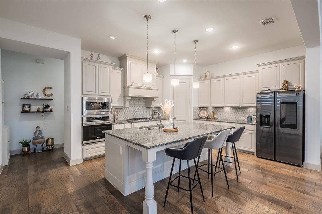 Open-concept kitchen featuring a large island with sturdy granite countertops, recessed lighting, pendant lighting, and stainless steel appliances