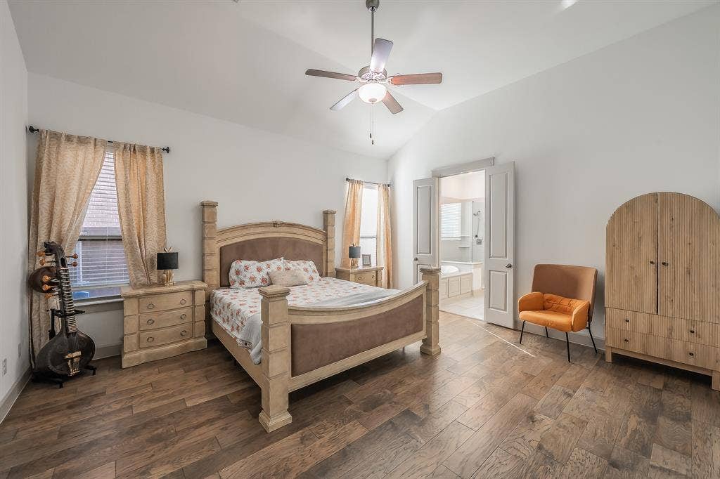 Vaulted ceiling with a ceiling fan, wood flooring, and double doors opening to an ensuite bathroom with a tub, separate shower, two sinks and a second closet