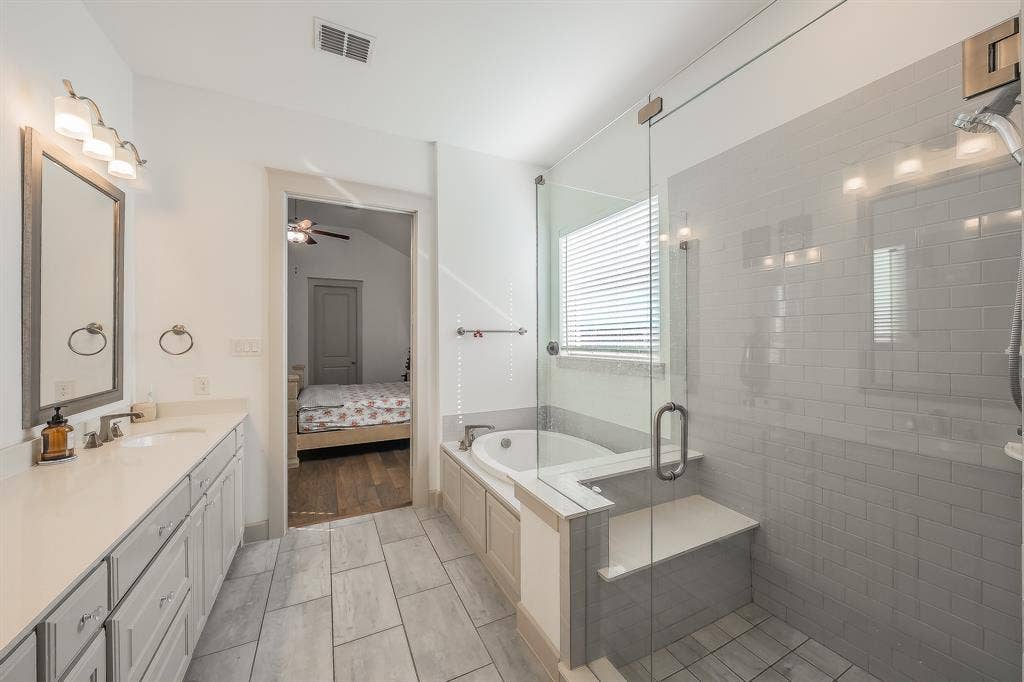Spacious bathroom with a walk-in shower featuring a bench and glass enclosure, a built-in bathtub, a double vanity with an undermount sink, and tile flooring