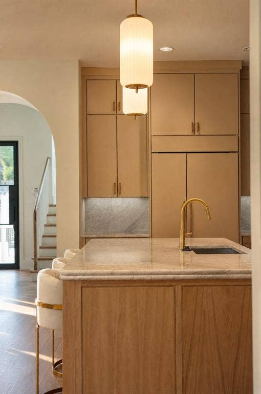 Kitchen island with natural wood-finish cabinetry, a stone countertop, and a gooseneck faucet
