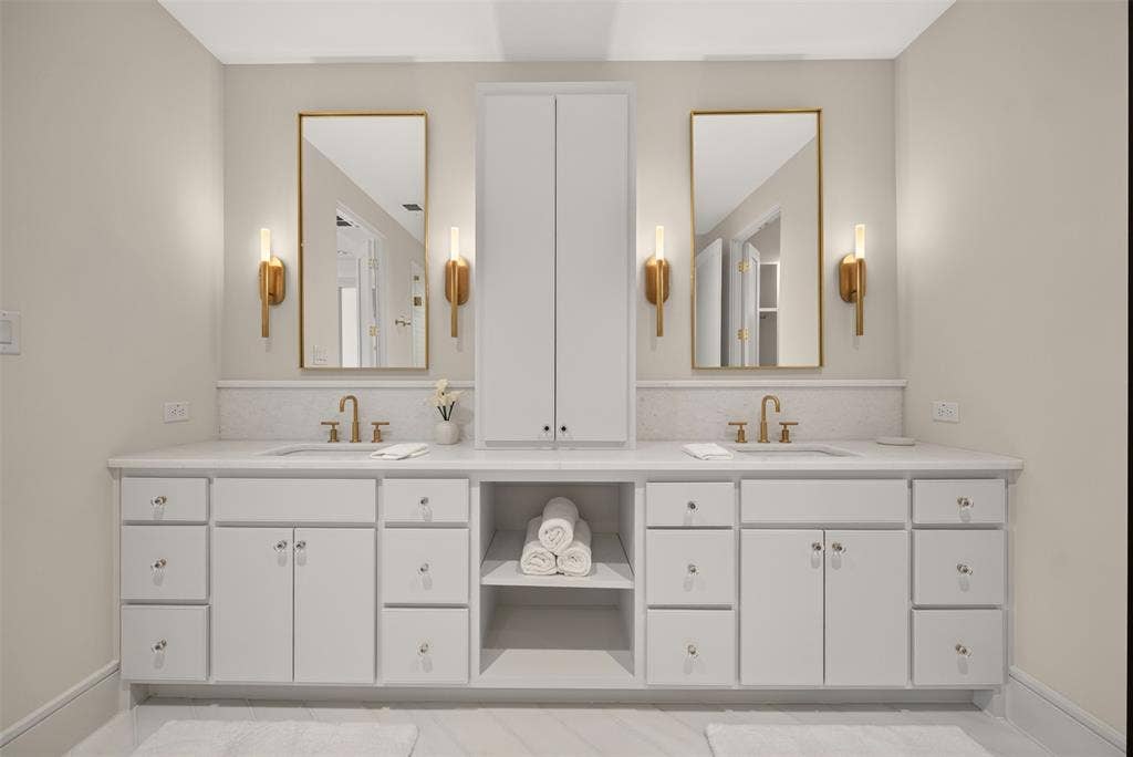 Dual vanity with white cabinetry, gold-finish hardware, rectangular undermount sinks, and wall-mounted sconces