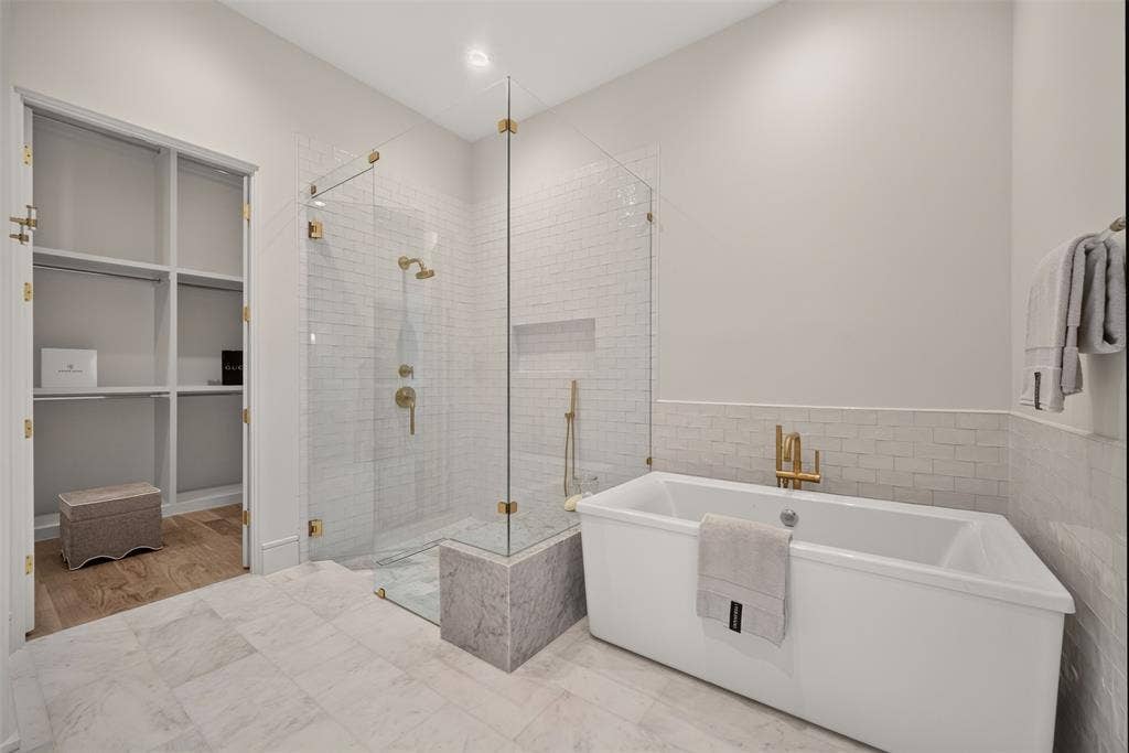 Freestanding soaking tub, glass-enclosed shower with subway tile, built-in shower bench, gold-finish fixtures, and a walk-in closet with built-in shelving