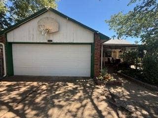 Attached garage with a white panel door, brick exterior accents, a basketball hoop, and a covered entryway