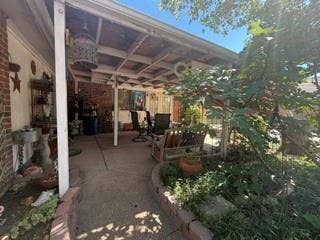 Covered patio with exposed wood ceiling beams, concrete flooring, and brick accent wall