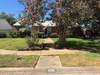 Brick exterior with a white front door and covered entryway, featuring a concrete walkway, mature landscaping, and an expansive front lawn