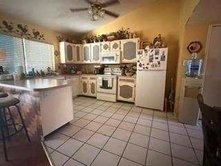Kitchen featuring white appliances, a breakfast bar with a decorative wood-finish facade, white cabinetry, and tile flooring