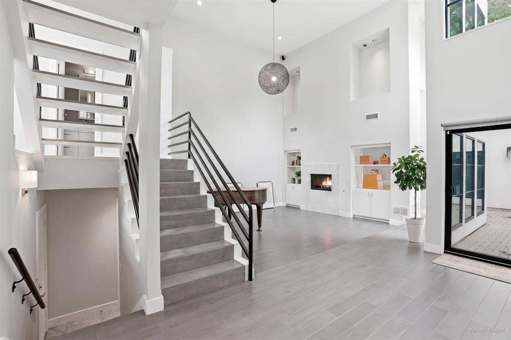 9123 Valley Chapel Lane, Dallas, TX 75220 Great room with soaring two-story ceilings, a marble gas fireplace flanked by built-in shelving, and an open staircase to the upper levels. Virtually staged.