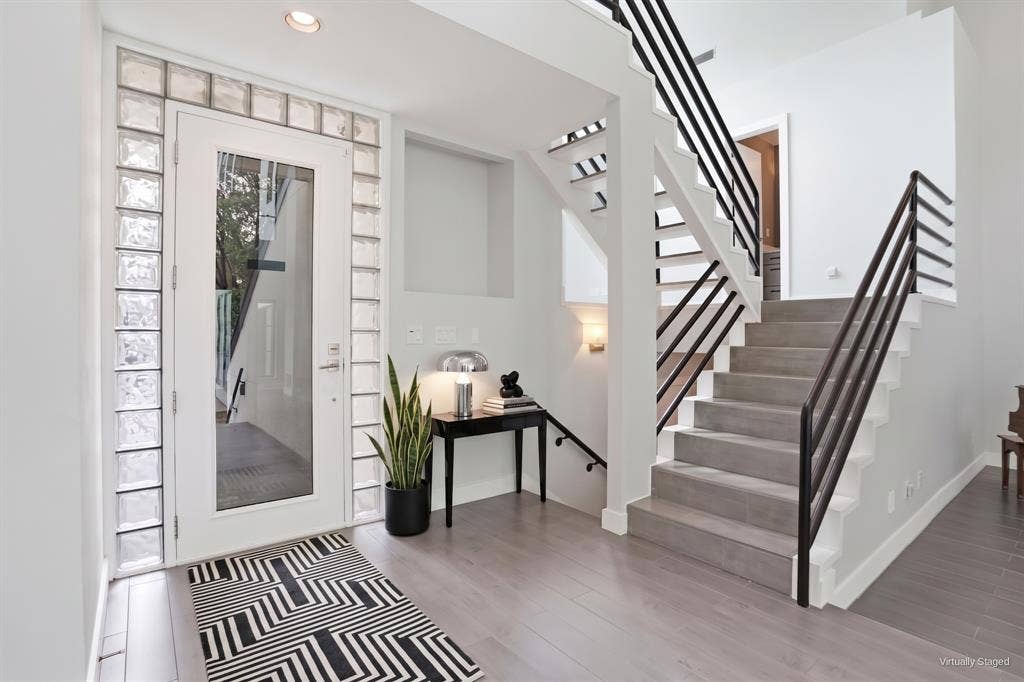 9123 Valley Chapel Lane, Dallas, TX 75220 Entry with glass-block sidelights and transom, a full-glass front door, and a floating staircase with black metal railings. Virtually staged.