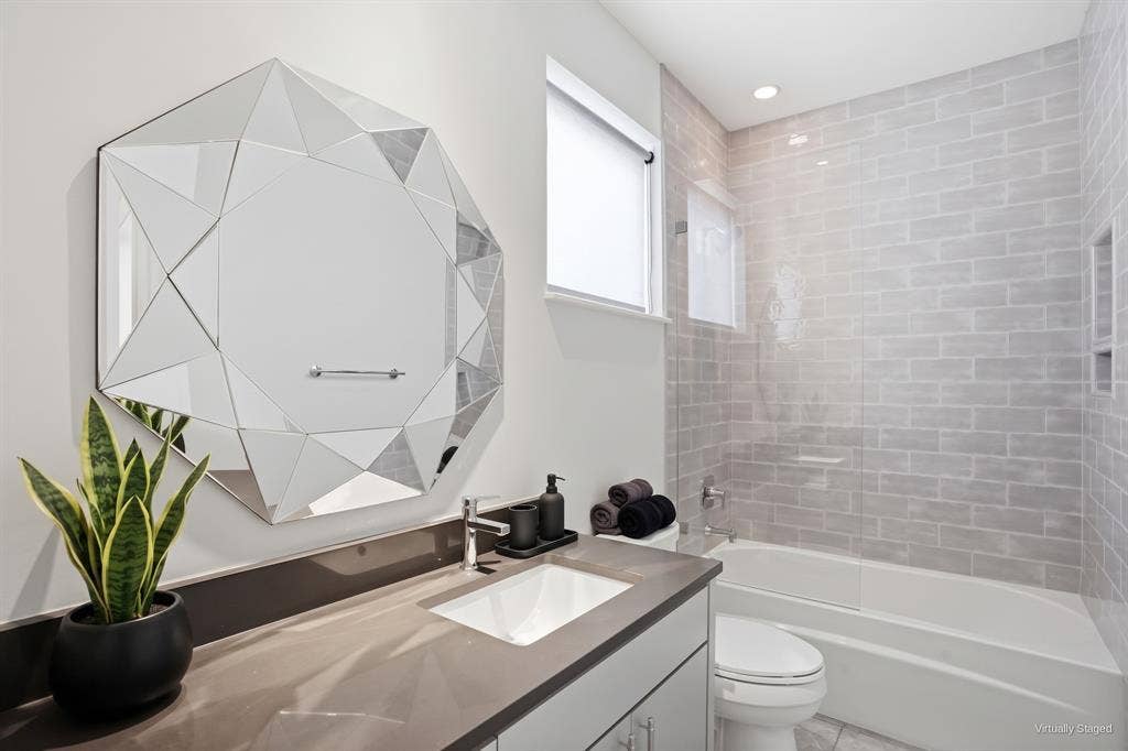 9123 Valley Chapel Lane, Dallas, TX 75220 Full bath with quartz vanity, tub and shower combo with glass panel, and gray tile surround with a built-in niche. Virtually staged.
