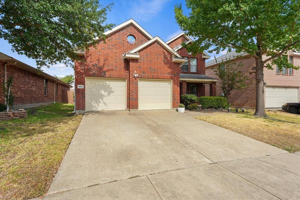 2053 Lake Trail Drive, Heartland, TX 75126 Brick facade residence featuring a two-car garage, concrete driveway, front porch, and mature trees