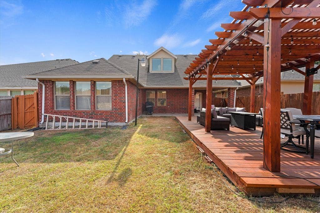 2053 Lake Trail Drive, Heartland, TX 75126 Expansive wood-finish deck with an attached pergola featuring string lighting, complemented by a brick exterior with multiple windows