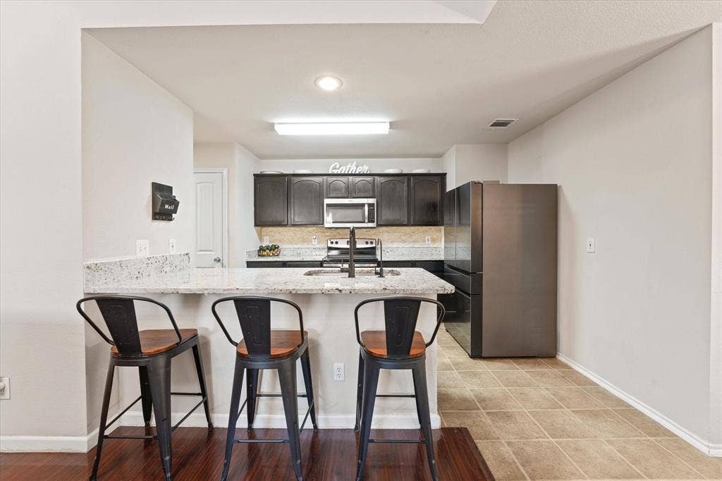 2053 Lake Trail Drive, Heartland, TX 75126 Kitchen featuring a peninsula with a light-colored countertop, dark wood-finish cabinetry, stainless steel microwave, black refrigerator, and tile flooring