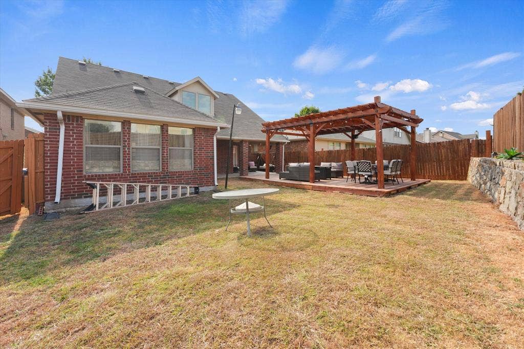 2053 Lake Trail Drive, Heartland, TX 75126 Expansive backyard featuring a wood pergola on a raised deck, a stone retaining wall, and a full privacy fence