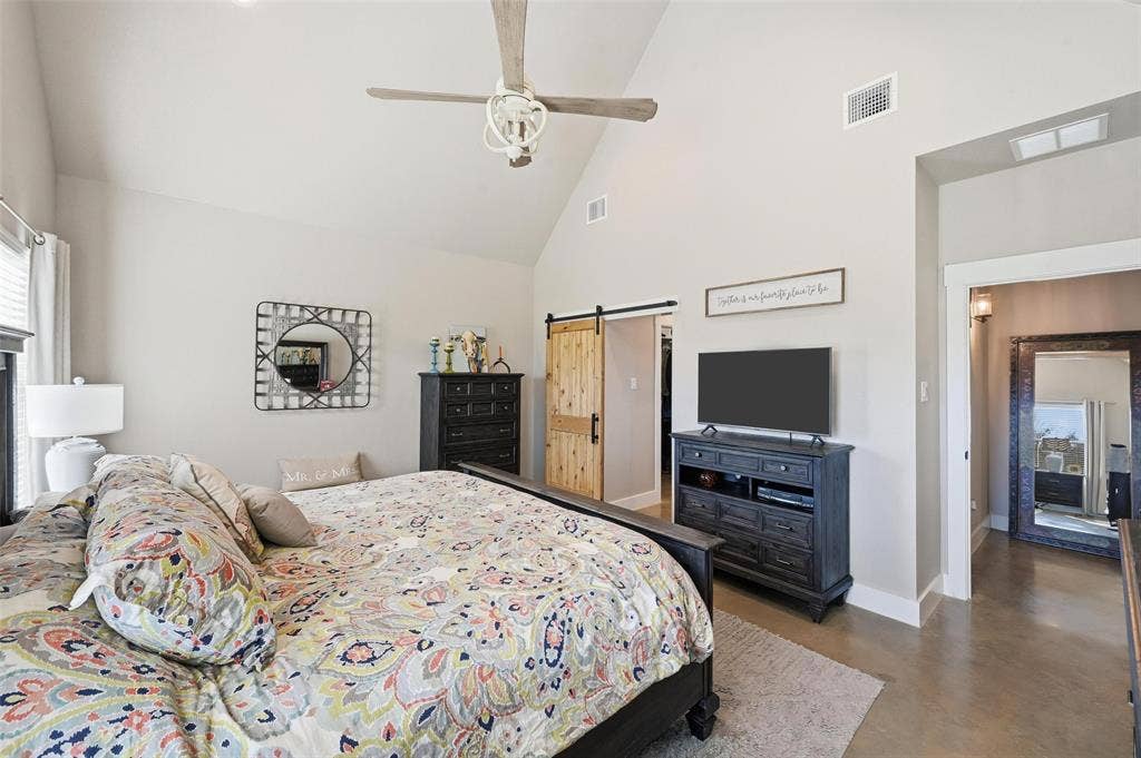 Bedroom featuring a barn door, high vaulted ceiling, finished concrete flooring, and ceiling fan
