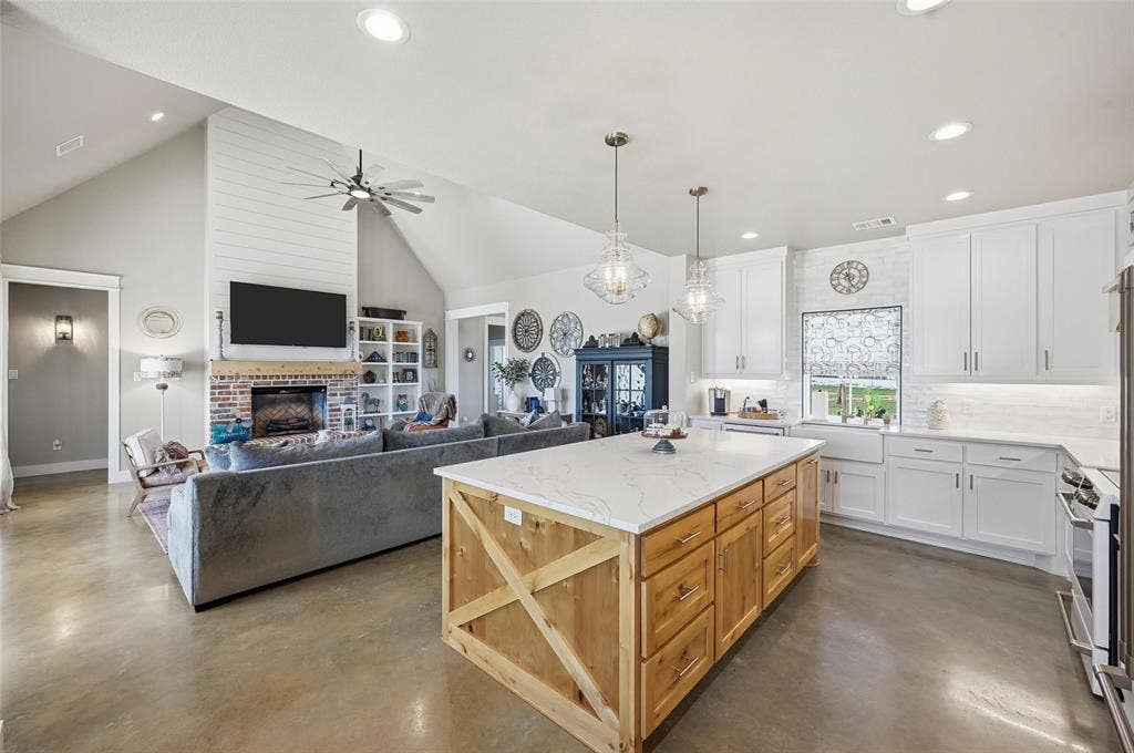 Kitchen featuring white cabinetry, a brick fireplace, concrete floors, decorative backsplash, and high vaulted ceiling