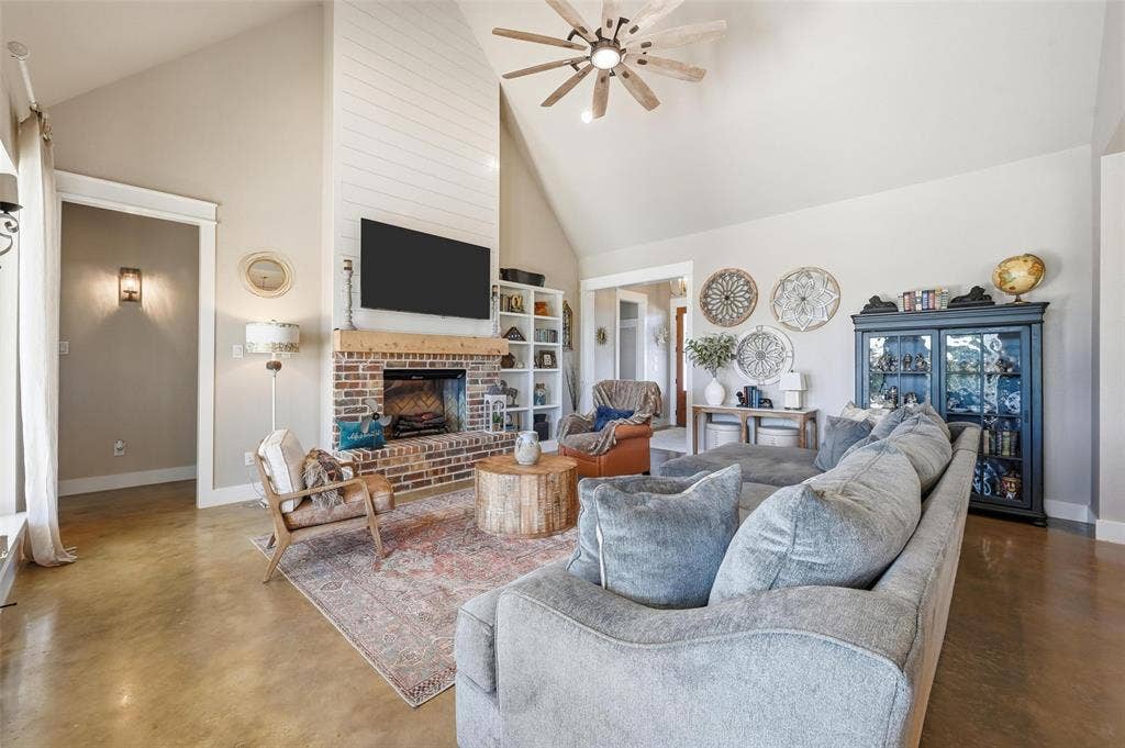 Living area featuring high vaulted ceiling, concrete flooring, ceiling fan, and a fireplace