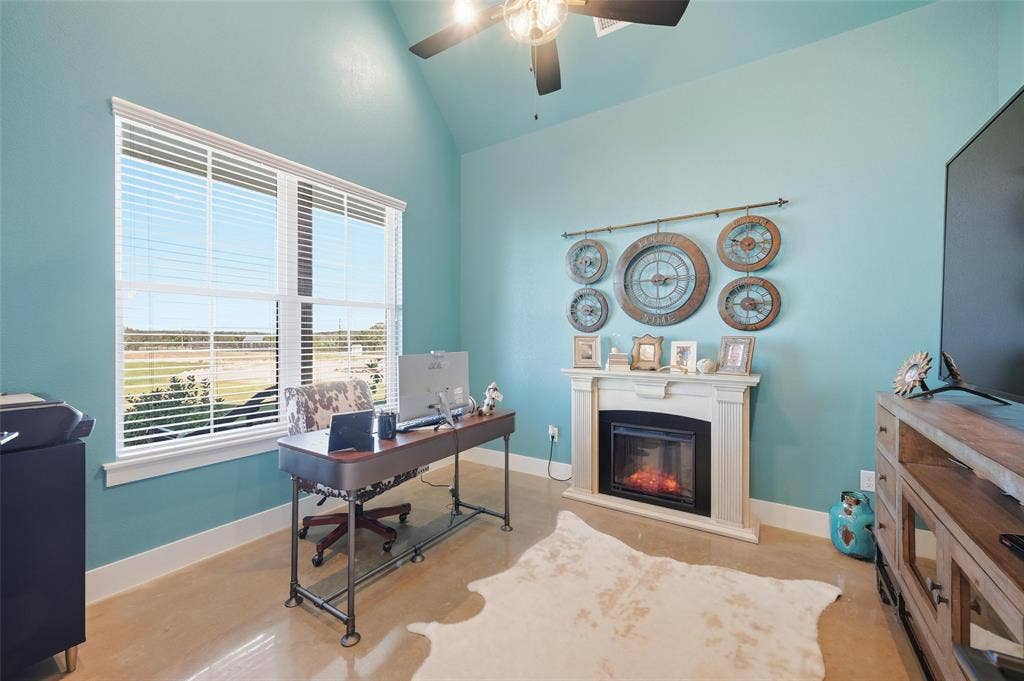 Home office featuring vaulted ceiling, a glass covered fireplace, and ceiling fan