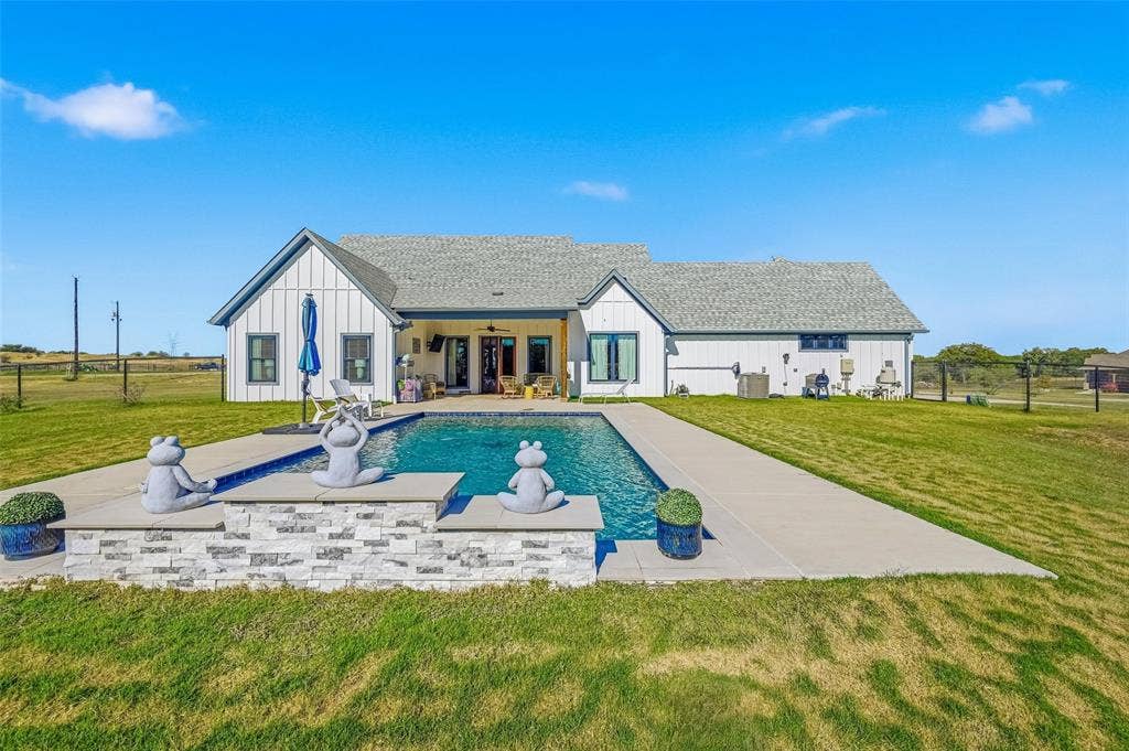 Rear view of house featuring board and batten siding, a covered patio area, an outdoor pool, and a shingled roof