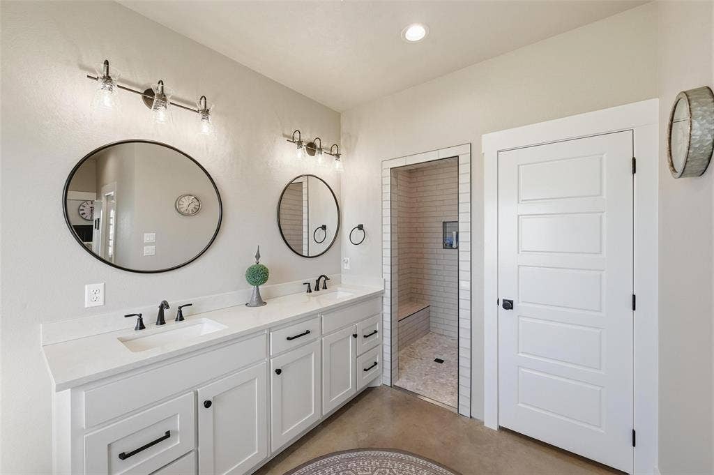 Primary Bathroom with double vanity, a walk in shower, recessed lighting, and finished concrete floors