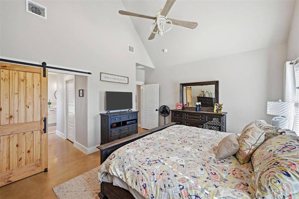 Bedroom with a barn door, high vaulted ceiling, ceiling fan, and ensuite bathroom
