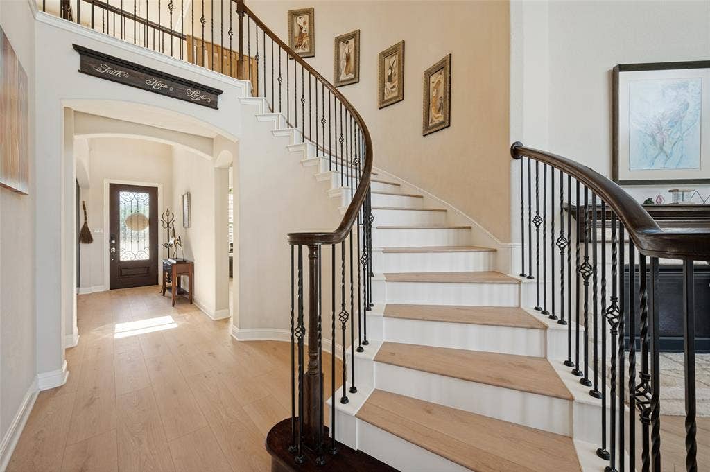 741 Darian Drive, Prosper, TX 75078 Grand foyer with light wood-finish flooring, a curved staircase featuring dark wood handrails and wrought iron balusters, and arched doorways
