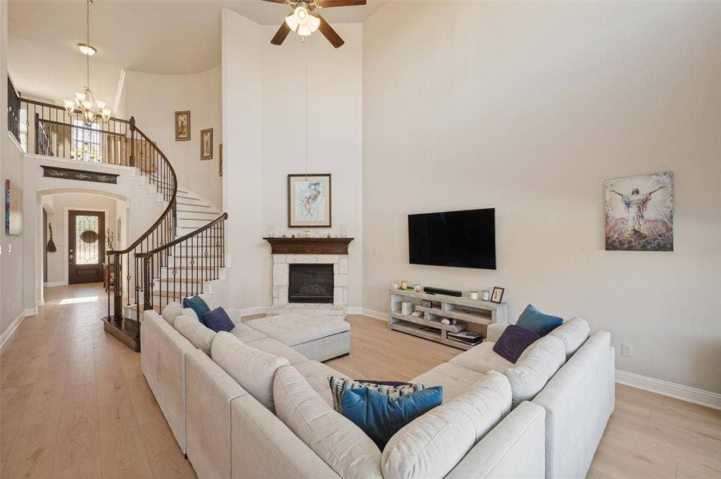 741 Darian Drive, Prosper, TX 75078 Two-story living area featuring a stone fireplace with wood mantel, a spiral staircase with wrought iron balusters, light wood-finish flooring, and a ceiling fan