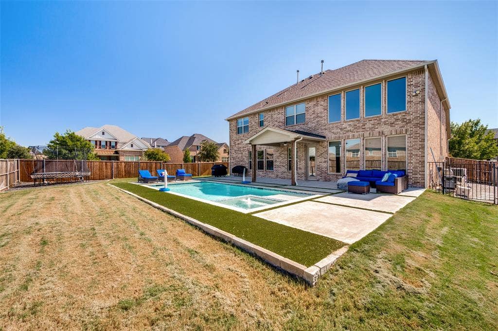 741 Darian Drive, Prosper, TX 75078 Brick exterior with multiple large windows, covered patio, fenced backyard, inground pool, and integrated spa
