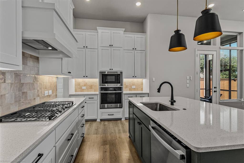 2601 Lafayette Drive, Rowlett, TX 75088 White shaker cabinetry, light-toned tiled backsplash, stainless steel appliances, large kitchen island with integrated sink, and wood-finish flooring