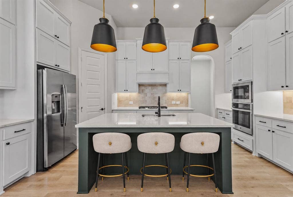2601 Lafayette Drive, Rowlett, TX 75088 Gourmet kitchen featuring a large central island with seating, stainless steel appliances, extensive white cabinetry, recessed lighting, and wood-finish flooring