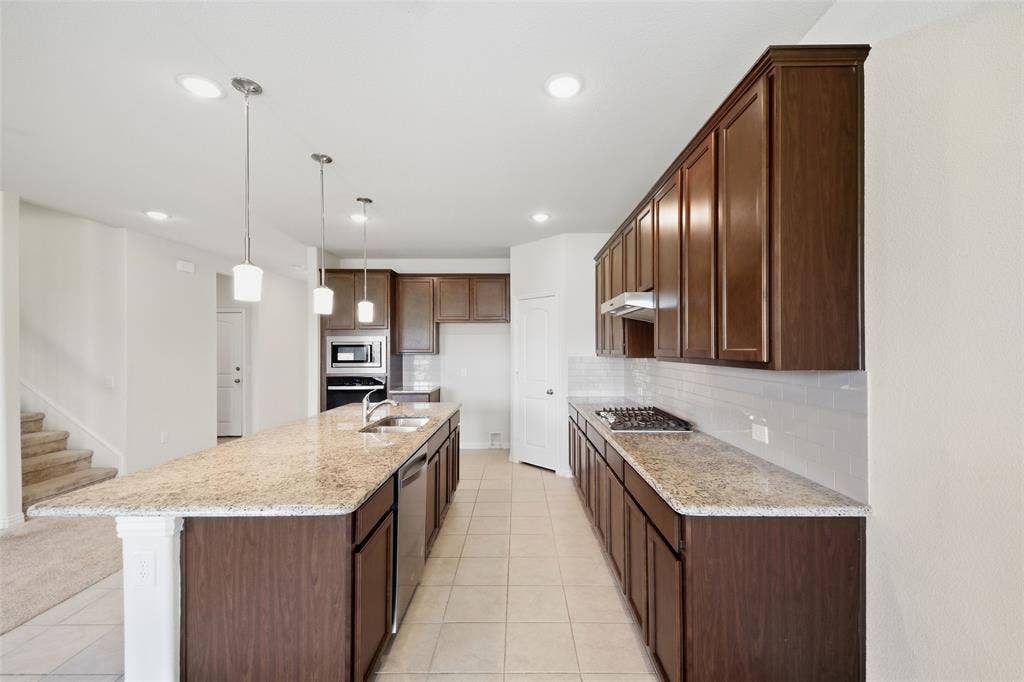 1805 Nelson Street, Anna, TX 75409 Kitchen featuring a long center island, dark wood-finish cabinetry, light-toned countertops, tile flooring, and integrated stainless steel appliances