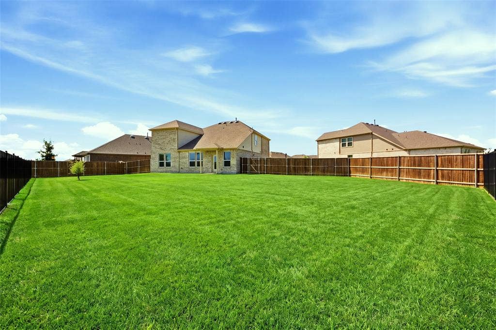 1805 Nelson Street, Anna, TX 75409 Expansive backyard featuring a manicured lawn, full wood fencing, and a two-story home with a stone and siding exterior