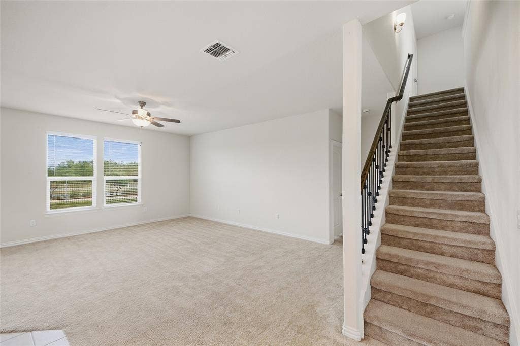 1805 Nelson Street, Anna, TX 75409 Open concept living area featuring dual windows, a ceiling fan with integrated lighting, and a carpeted staircase with dark iron balusters
