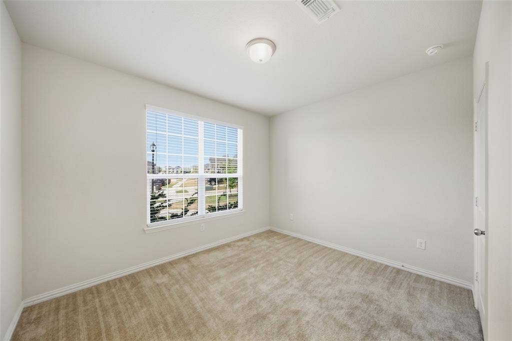 1805 Nelson Street, Anna, TX 75409 Carpeted room featuring a large window with blinds, ceiling-mounted light fixture, and neutral wall tones