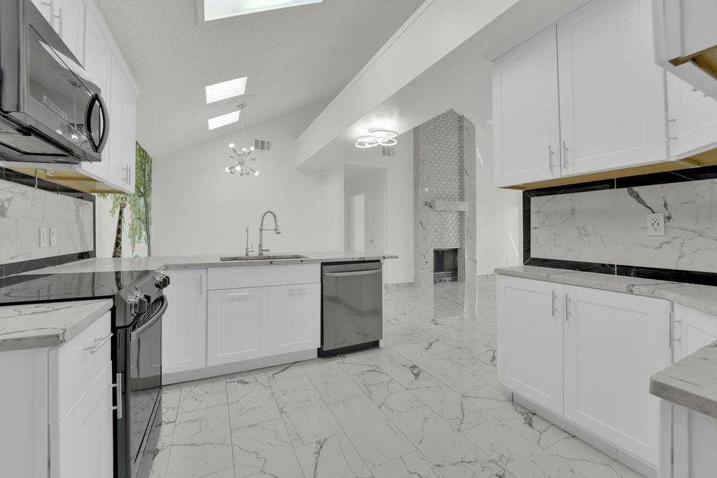 Vaulted ceiling with skylights, white cabinetry, integrated stainless steel appliances, light-toned flooring, and a decorative fireplace