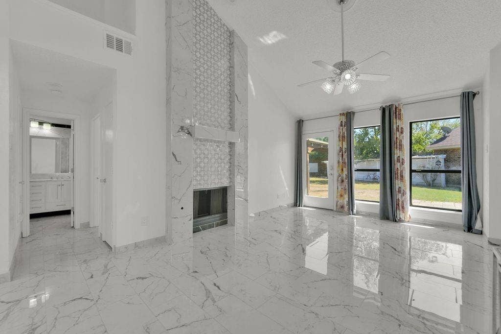 Vaulted ceiling with a ceiling fan, fireplace with a decorative surround, large windows, and reflective tile flooring