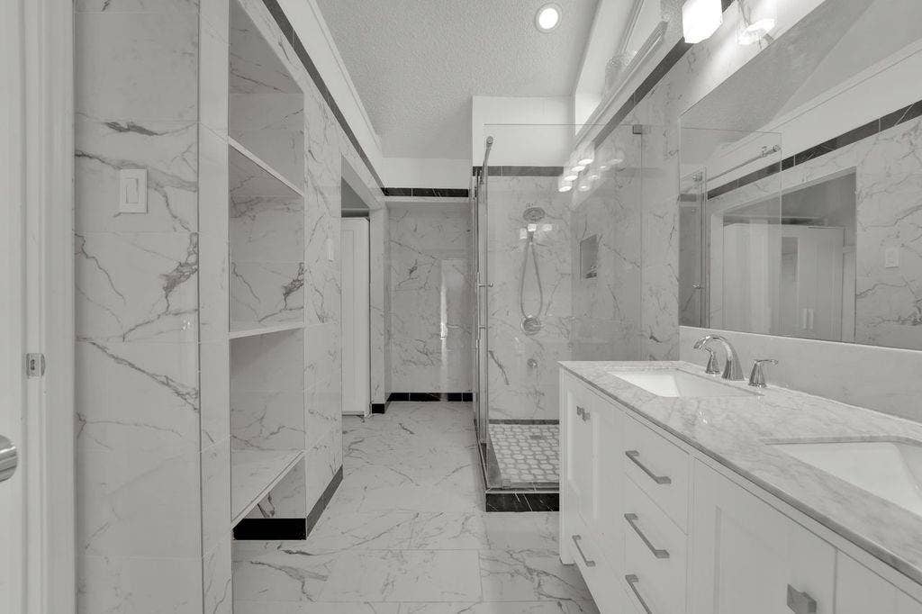 Dual vanity with integrated sinks, full-width mirror, glass-enclosed shower, and built-in shelving