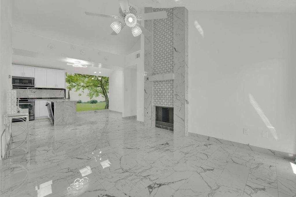 Vaulted ceiling with an attached ceiling fan, floor-to-ceiling fireplace with decorative tile accents, large format tile flooring, white cabinetry, and a kitchen island with a built-in dishwasher