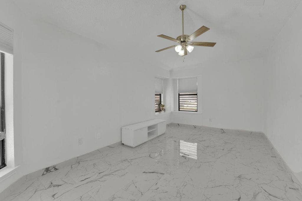 Recessed window with horizontal blinds, polished tile flooring with natural stone-look veining, and a ceiling fan with light fixture