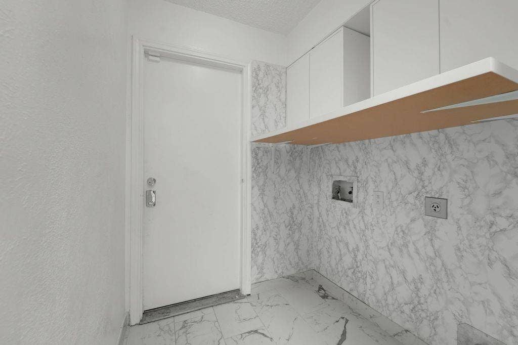 White cabinetry with a white countertop and marble-look wall and floor tile