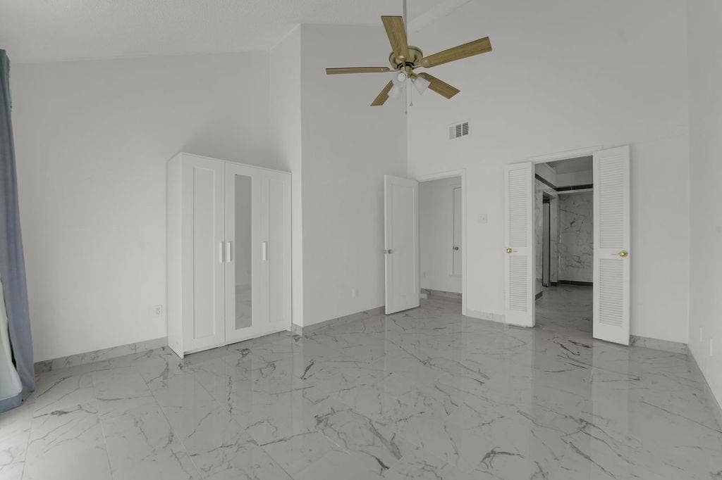 Vaulted ceiling with ceiling fan, white paneled doors, and polished tile flooring