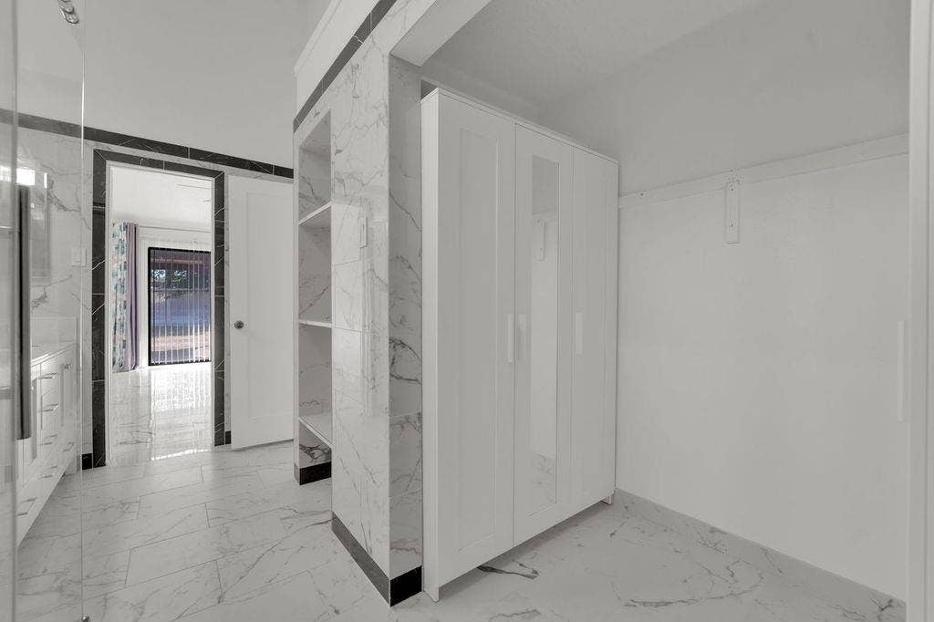 White marble-look floor tiles, built-in shelving, white door, and white painted walls