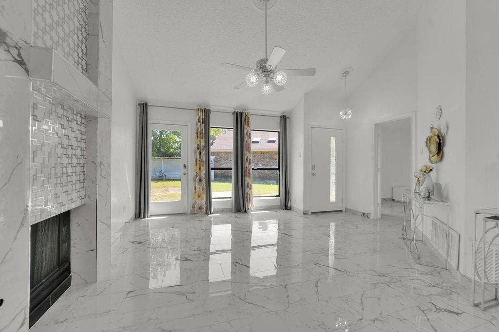 High-gloss tile flooring, vaulted ceiling, decorative fireplace with tile surround, ceiling fan, and transom windows