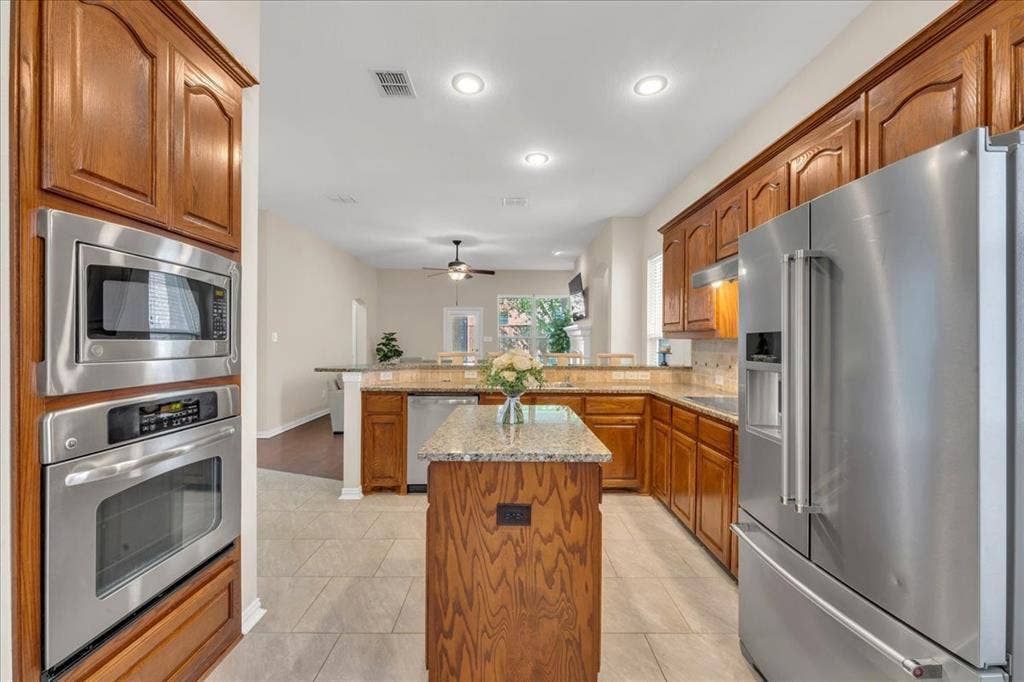 5612 Hampshire Drive, McKinney, TX 75070 Kitchen featuring wood cabinetry, stainless steel appliances, a center island with a stone countertop, and tile flooring