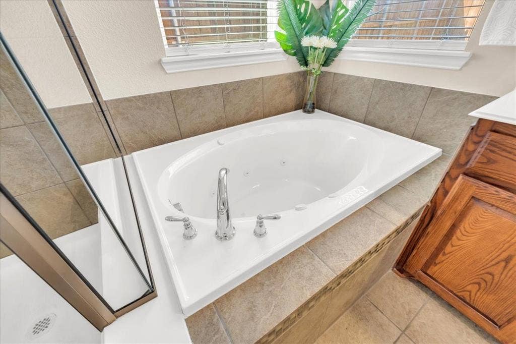 5612 Hampshire Drive, McKinney, TX 75070 Corner soaking tub with polished chrome fixtures, tile surround, and adjacent glass-enclosed shower