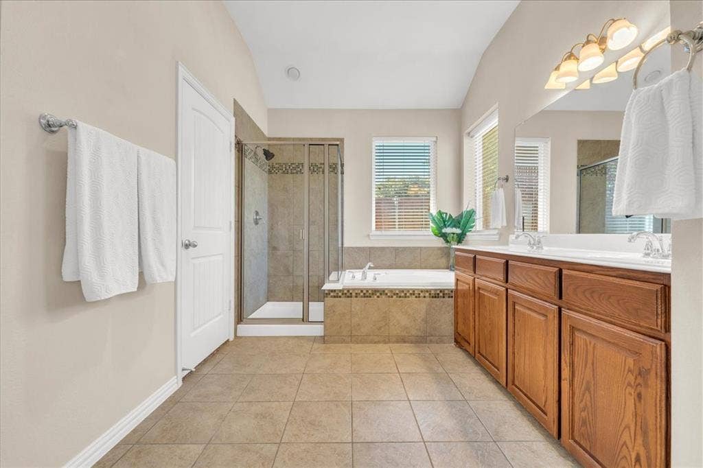 5612 Hampshire Drive, McKinney, TX 75070 Spacious bathroom featuring a dual vanity with wood-finish cabinetry, a tiled soaking tub, a separate glass-enclosed shower, and tile flooring