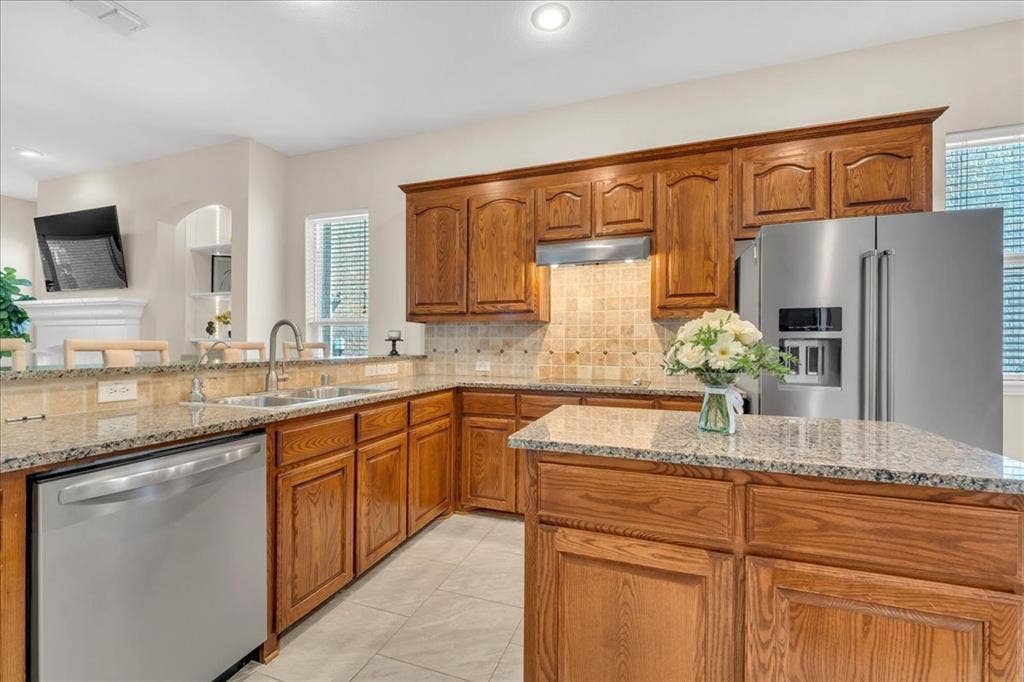5612 Hampshire Drive, McKinney, TX 75070 Kitchen featuring wood cabinetry, stainless steel appliances, granite countertops, tile backsplash, and a central island